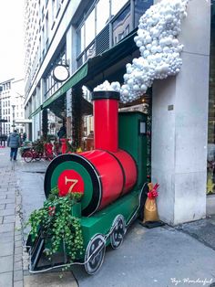 a green and red train is parked on the side of the street next to a building