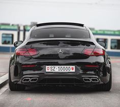 the rear end of a black mercedes s - class coupe parked in front of a train station