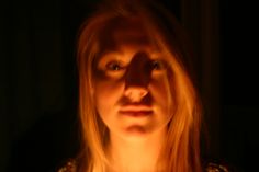 a woman is looking at the camera with an intense look on her face as she holds a lit candle in front of her face