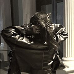 a woman in a leather jacket is sitting on a bench with her back to the camera