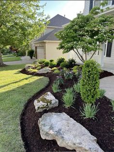 landscaping in front of a house with rocks and flowers on the ground, grass and trees