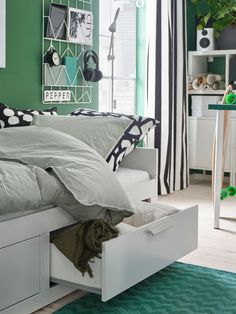 a bedroom with green walls and white bedding has drawers under the bedspread