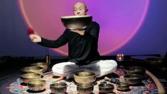 a man sitting on top of a table with lots of singing bowls in front of him