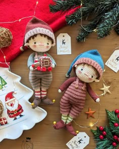 two knitted dolls sitting on top of a wooden table next to christmas decorations and ornaments