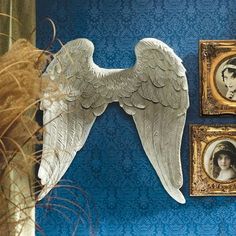 an angel wing is hanging on the wall next to two framed pictures and a plant