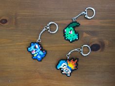 three pixel key chains are sitting on a wooden surface, one has an image of mario and the other is a video game character