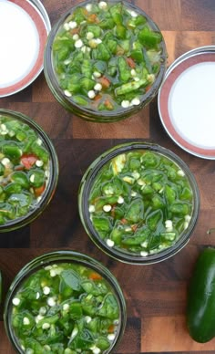 four glass jars filled with green vegetables on top of a wooden table