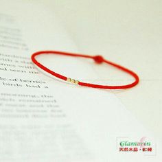 a red string bracelet with two gold beads on top of an open page of paper