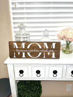 a wooden sign that says mom on top of a white dresser next to a vase with flowers