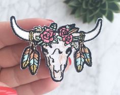 a hand holding a flower decorated bull skull pin