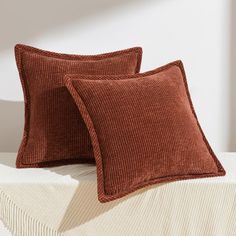 two brown corded pillows sitting on top of a white bed next to each other