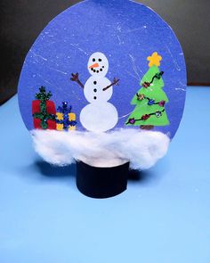 a snow globe with a christmas tree and a snowman in it on a blue surface