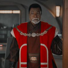 an older man in a star wars outfit holding his hand up to the side while standing next to a door