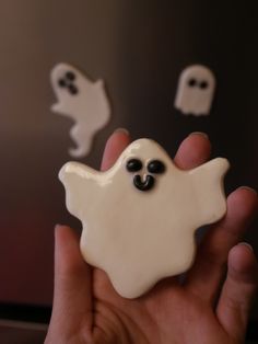 a hand holding a small white button with black eyes and ghost faces on it's side