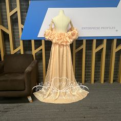 a dress on display in front of a wall with a sign and chair behind it