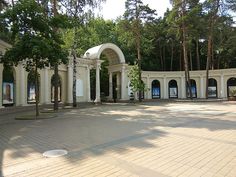 an empty plaza with trees and benches on the side walk, surrounded by white arches