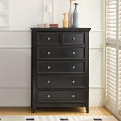 a black dresser sitting next to a window with shutters on both sides and vases on top