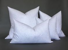 three white pillows stacked on top of each other in front of a gray background,