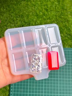 a hand holding a plastic container filled with ice cubes on top of a green surface