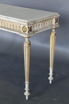 an antique white and gold painted table with ornate carvings on the top, sitting against a gray background