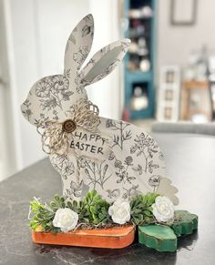 a white rabbit sitting on top of a table next to some flowers and greenery