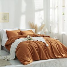 a bed with an orange comforter and white sheets in a room next to a window