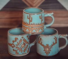 four coffee mugs sitting on top of a table next to each other with designs painted on them