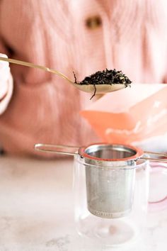 a person is holding a spoon with some tea on it and there are two cups in front of them