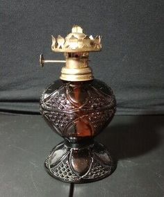 an antique brass and glass oil burner with a crown on top, sitting on a black surface