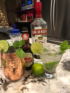 two glasses filled with green liquid and limes sitting on a counter next to bottles