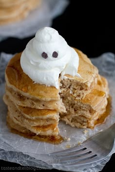 a stack of pancakes topped with whipped cream and a ghost face cut out of it