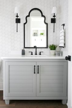 a bathroom vanity with two sinks and a large mirror above it, in front of a patterned wallpapered wall