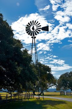 a windmill in the middle of a field with trees and grass around it on a sunny day