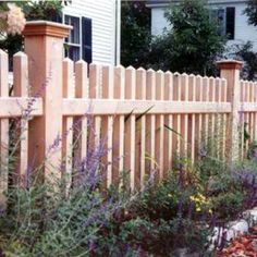 a wooden fence in front of a house with purple flowers growing on the side walk