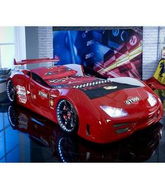 a red race car bed sitting on top of a black floor next to a window