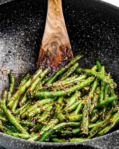 green beans are being cooked in a wok with a wooden spoon on the side