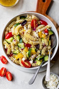 a white bowl filled with pasta salad next to two spoons