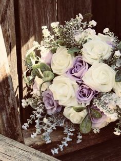 a bouquet of white and purple flowers sitting on top of a wooden bench next to a fence