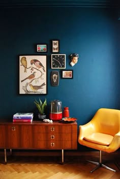 a living room with blue walls and a yellow chair next to a wooden dresser in the corner