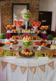 a table topped with lots of different types of fruit and desserts next to a brick wall