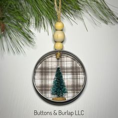 a glass ornament with a christmas tree on it hanging from a pine tree