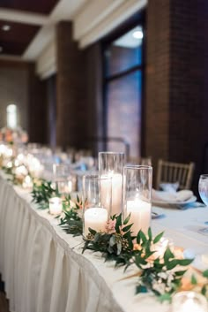 a long table with candles and greenery on it is set up for a formal function