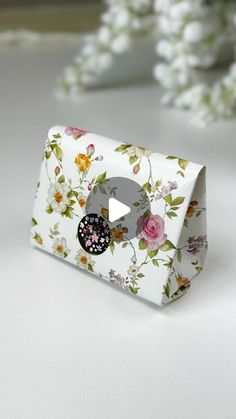 a white box with flowers on it and a black button in the middle is sitting on a table