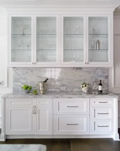 a kitchen with white cabinets and marble counter tops, along with wine glasses on the shelves