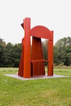 a large red sculpture sitting on top of a lush green field