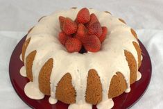 a bundt cake with white icing and strawberries on top is sitting on a red plate