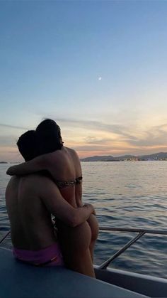 two people sitting on the back of a boat in the water at sunset or dawn