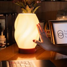 a woman's hand is on top of a table next to a lamp that looks like a vase