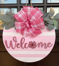 a welcome sign hanging from the side of a door with a pink bow on it