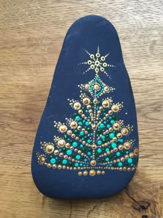 a blue rock with a christmas tree painted on the front and sides, sitting on a wooden surface